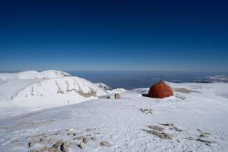 Verrostetes Biwak auf einem schneebedecktem Gipfel, Blick ins Flachland bis zur Adriaküste.