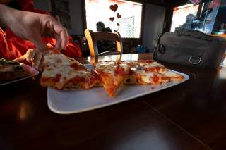 Hände greifen nach Pizzastücken auf einem Teller.