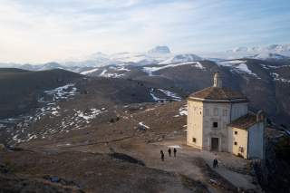 Alte Kapelle vor einer Hochebene, im Hintergrund verschneite Gipfel.