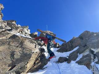Mensch mit Ski am Rucksack klettert felsige Schlüsselstelle ab