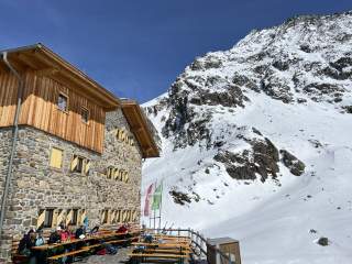 Hüttenterrasse in der Sonne, verschneite Berge im Hintergrund