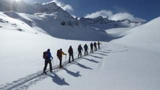 Eine Gruppe von Menschen läuft auf Tourenski durch verschneite Winterlandschaft
