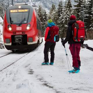 Zwei Menschen mit Skiausrüstung warten auf einfahrenden Zug