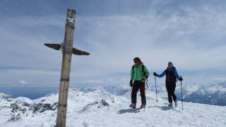 Skitourengeherin und Skitourengeher am Gipfelkreuz auf der Cima Marmotta