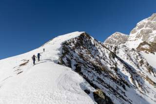 Drei Skitourengeher im Aufstieg über einen breiten Bergrücken