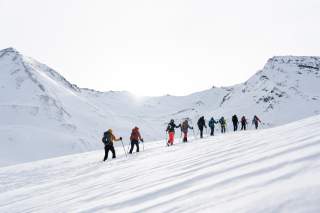 Viele Menschen in einer Reihe unterwegs auf einer Skitour in Richtung Breite Krone. Rundherum verschneite Berge.