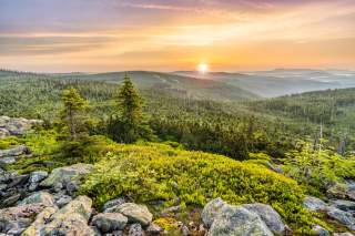 Die Sonne geht über dem Bayerischen Wald auf. Im Vordergrund die Felsen des Lusen-Gipfels.