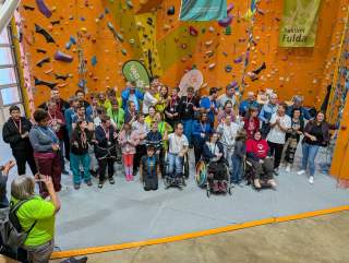 Gruppenfoto von Menschen mit und ohne Behinderung vor einer Kletterwand, einige tragen Medaillen und Ausweise, eine Person fotografiert die Gruppe. Im Hintergrund sind Banner der Sektion Fulda und Special Olympics zu sehen.