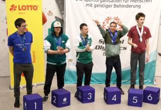 Fünf Kletterer mit Behinderung stehen bei der Siegerehrung hinter ihren Rängen