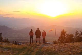 Drei Menschen stehen am Berg und genießen den Sonnenuntergang.
