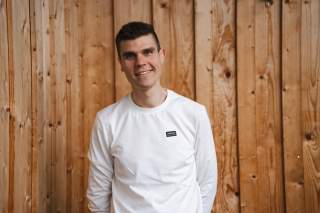 Porträt Jakob Roithmeier vor Holzwand. Er trägt ein weißes Langarmshirt.