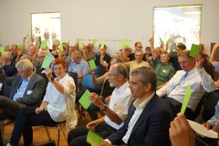 Menschen sitzen in Raum und stimmen mit grünen Zetteln ab