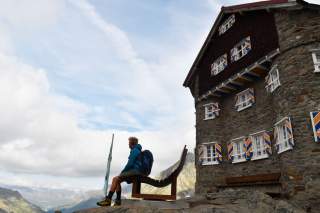 Wanderer sitzt auf Bank vor Berghütte