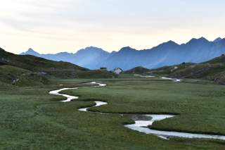 Hütte vor Wiese mit mäanderndem Bach
