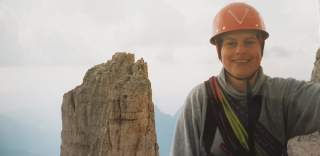 Portrait einer Bergsteigerin mit Helm vor einem Felsturm der Dolomiten.