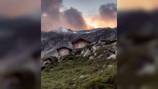 Almhütten vor felsigem Hochgebirge, Gewitterstimmung