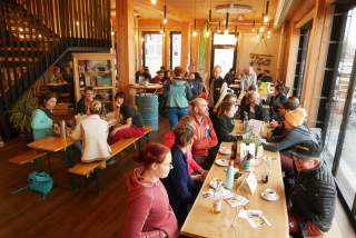 Seminarteilnehmer sitzen in geselliger Runde an großen Tischen in einer Caféteria mit viel Holz und Glas.