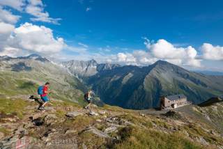 Zwei Menschen wandern auf Höhenweg Richtung Hütte