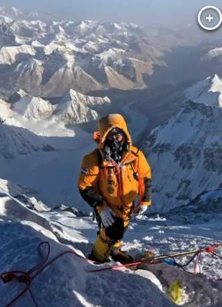 Frau in gelbem Expeditionsanzug auf dem Weg zum Mount Everest. Im Hintergrund überall weiße Gipfel.