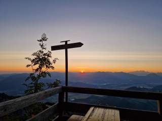 Wegweiser auf Hüttenterrasse, im Hintergrund geht die Sonne unter