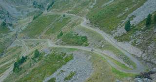 Bergweg zieht sich durchs Bild, zwei Menschen auf Mountainbikes fahren darauf bergab