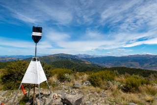 Eine schwarz-weiß markierte Metallmarkierung auf einem Berggipfel, die entfernt an eine Pyramide erinnert.