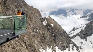 Auf der Aussichtsplattform am Kitzsteinhorn in Kaprun hält eine Frau einen Jungen auf dem Arm. Im Hintergrund ragen die hohen Tauerngipfel in den Himmel.