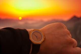 Sonnenaufgang in den Bergen, davor: Handgelenk mit einer Uhr, die 5:50 zeigt.