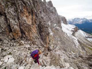 Eine Wanderin geht in die Hocke, um auf einem für sie schwierigen Bergweg in den Dolomiten abzusteigen.