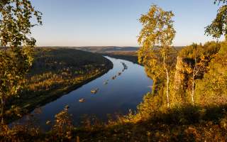 Blick von einer Anhöhe in herbstlich verfärbte Landschaft. Ein Fluss beschreibt eine Schleife durch waldbewachsene Hänge.