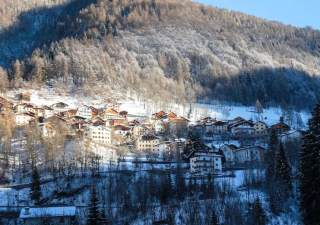 Ein verschneites Bergdorf an einem etwas verschatteten, winterlichen Hang.