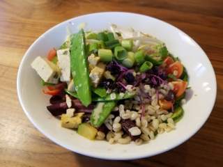 Vegane Bowl von der Brunnsteinhütte. Auf einem Holztisch steht eine Bowl mit knackig-frischen Zutaten.
