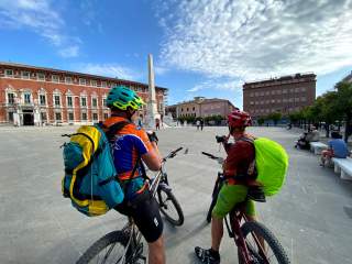 Zwei Mountainbiker stehen auf einem Platz vor einem historischen Palast.