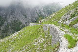 Zwei Mountainbiker fahren auf einem aus groben Steinen angelegten Bergweg.