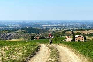 Mountainbiker auf einem ansteigenden Feldweg, im Hintergrund besiedeltes Flachland