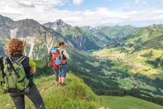 Drei Bergwanderer (1 Mann, 2 Frauen) schauen an einem Sommertag von einem Gipfel ins Tal.