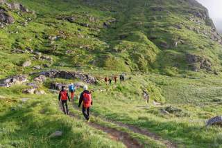 Eine Gruppe Wanderer auf einem einfachen Weg vor einem grasgrünen Berg