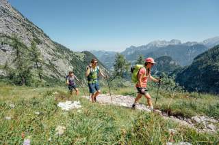 Drei Menschen wandern bei Sonnenschein am Berg