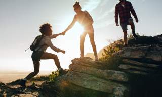 Frau reicht anderer Frau die Hand beim Wandern Frau reicht anderer Frau die Hand beim Wandern