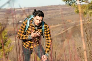 Ein junger Mann fasst sich beim Wandern an den schmerzenden Brustkorb