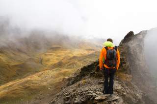 Ein junger Mann wandert an einem ausgesetzten Stelle durch die nebelverhangenen Berge.