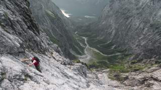 Mensch steigt felsige Wand hinauf, Blick hinab auf See