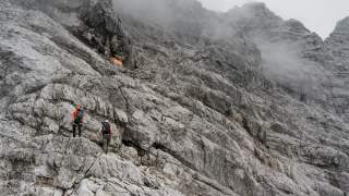 Zwei Menschen wandern in Felsenmeer auf orangenes Biwak zu