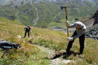Zwei Männer arbeiten mit Spitzhacke an Bergweg