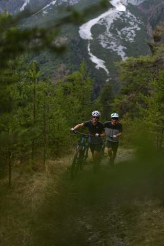 Zwei Menschen schieben ihre Mountainbikes steilen Weg hoch