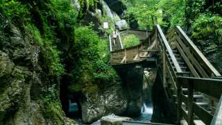Treppen die in einer Klamm über Wasser führen, an grün bewachsenen Felsen vorbei.