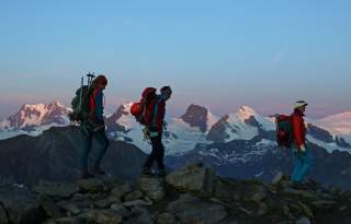 Drei Bergsteiger steigen im Morgengrauen zum Zwischenbergpass auf.