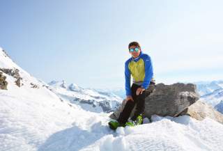 Mann sitzt auf Stein im Schnee