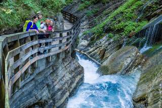 Vier Personen stehen an Holzgeländern und bewundern tosendes Wasser in einer Klamm