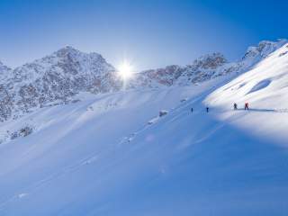 Der Expedkader im Aufstieg mit Skiern vor schönstem Bergpanorama.